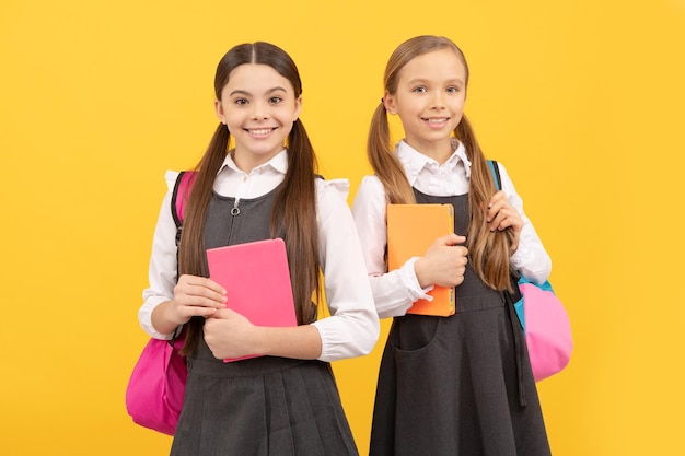 Happy kids in fomal uniforms with study books carry school bags yellow background knowledge