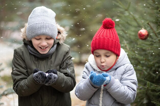 写真 雪に覆われた冬の森で雪を吹いて野外で遊んでいる幸せな子供たち ⁇ 女の子と男の子 ⁇