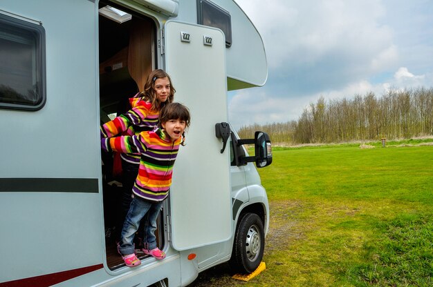 Happy kids near camper (RV) having fun, family vacation trip in motorhome