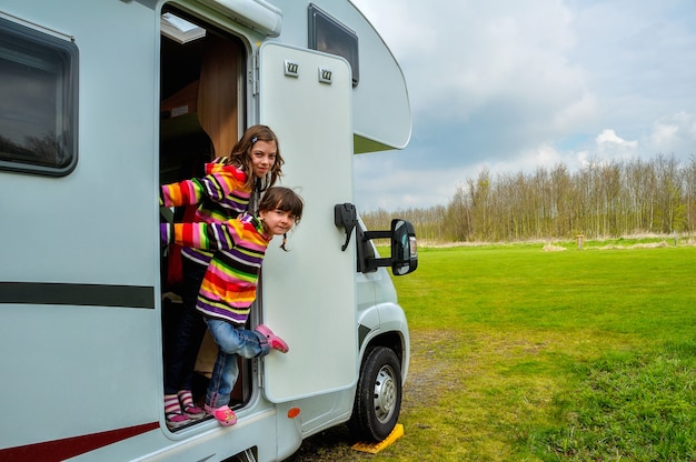 Happy kids near camper (RV) having fun, family vacation trip in motorhome