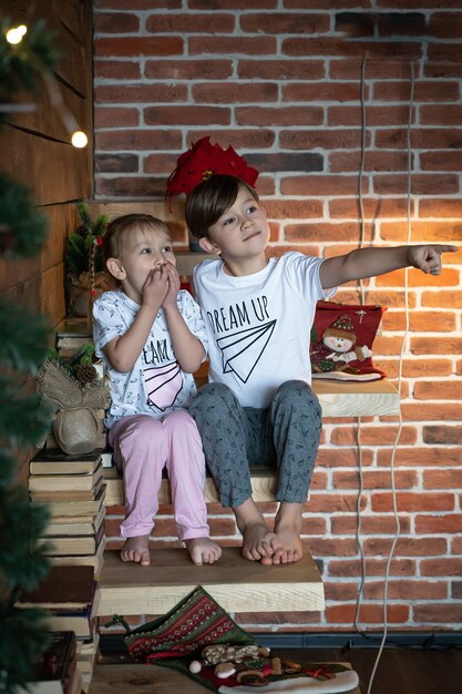 Happy kids in pajamas pointing finger up reaching above copy space. Merry christmas concept new year