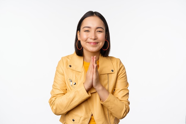 Happy korean woman looking hopeful asking for help favour begging standing with namaste gesture and smiling standing over white background