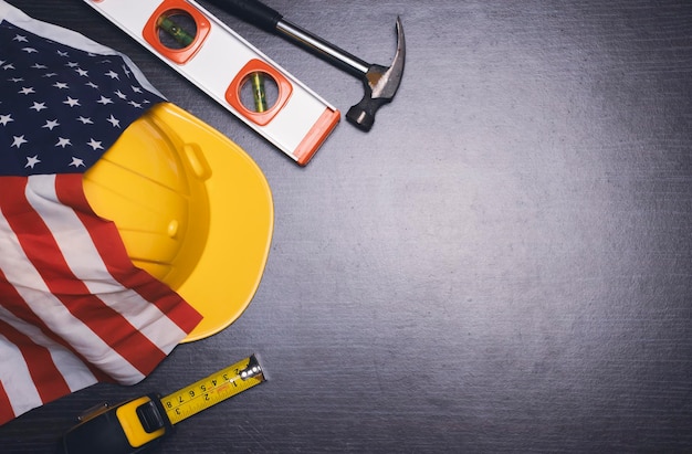 Happy labor day concept with american flagsafety hatlevelhammermeasuring tape on wooden background and copy space