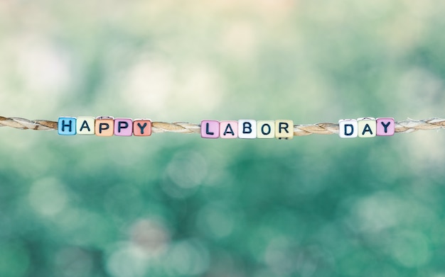 Photo happy labor day word hanging by rope with beautiful green nature bokeh background