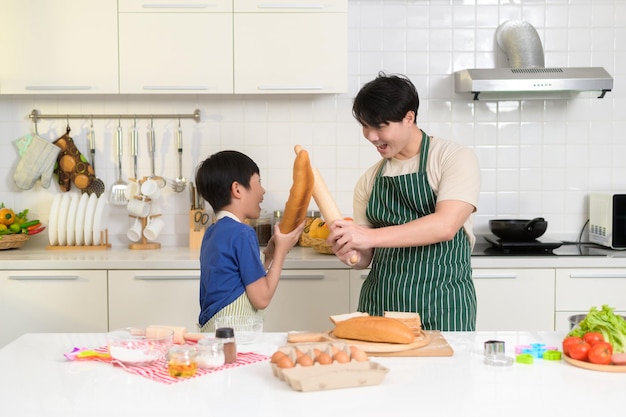 Happy lachende jonge Aziatische vader en zoon koken in de keuken thuis