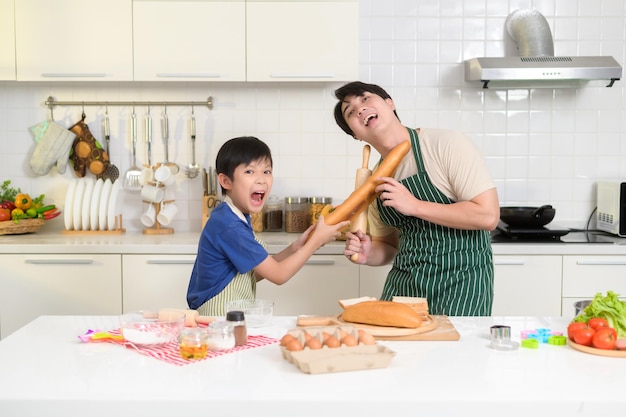 Happy lachende jonge Aziatische vader en zoon koken in de keuken thuis