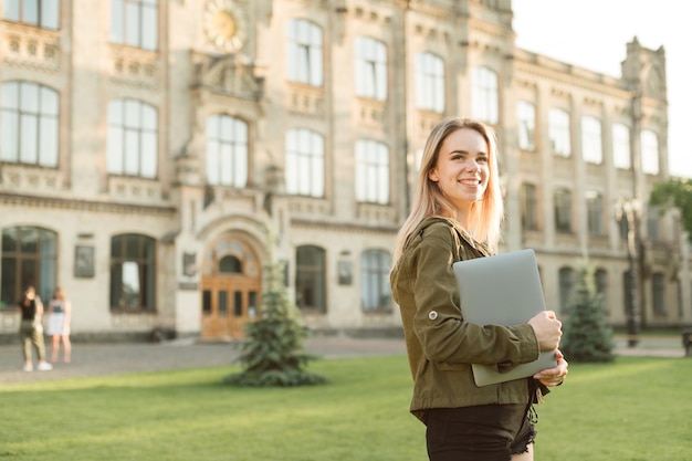 Photo happy lady in casual clothes standing on grass in campus on background of university building