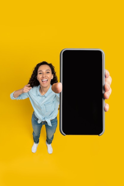 Happy lady showing blank mobile phone screen at studio