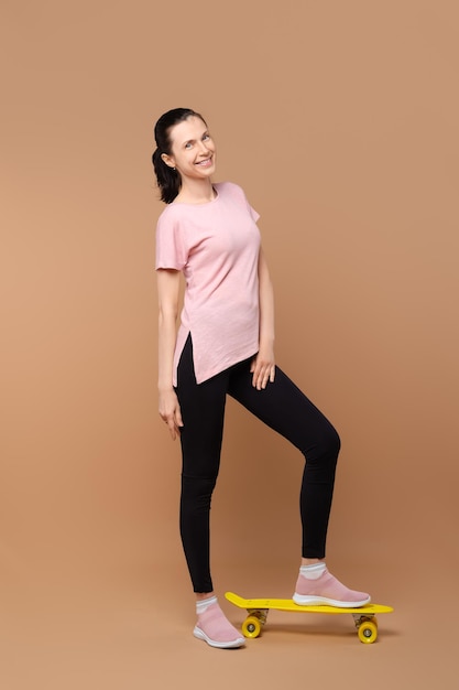 Happy lady in sportive outfit posing in studio with skateboard