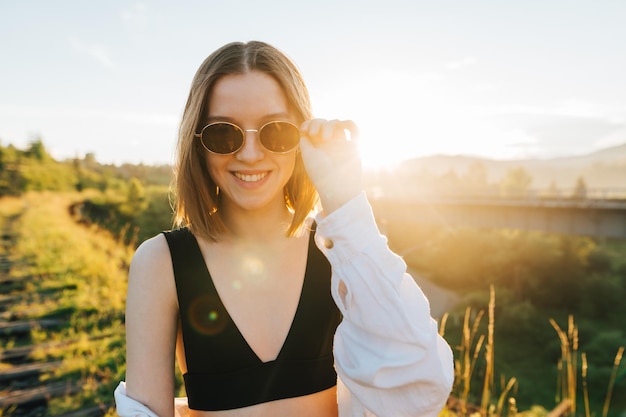 Happy lady tourist in casual clothes stands on the old bridge against the backdrop of the sunset