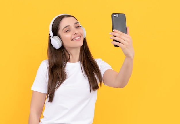 Happy lady in white shirt in headphones making selfie on phone gadget