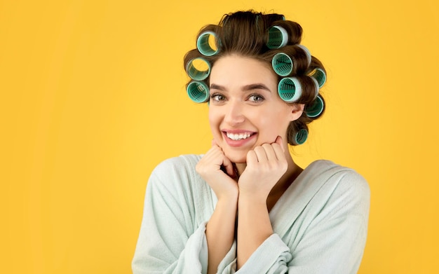 黄色の背景の上にポーズを笑顔ヘアカーラーと幸せな女性