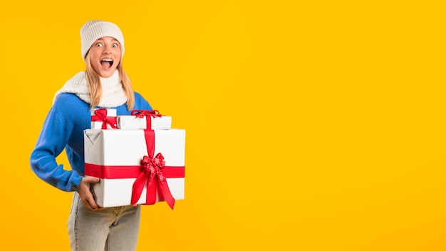 Happy lady with stack of xmas boxes standing over yellow studio background panorama free space