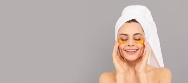 Happy lady with terry towel use facial golden eye patch for skin spa Beautiful woman isolated face