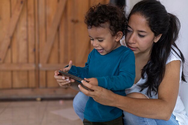 Happy Latin American mom 30 and son 2 are sharing a moment while using a cell phone Mother39s Day concept and technology