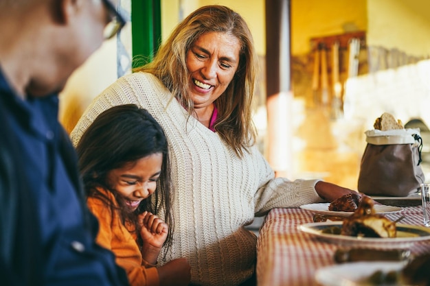 Foto felici nonni latini che si divertono a mangiare con la nipote nel patio di casa concentrati sul viso della nonna