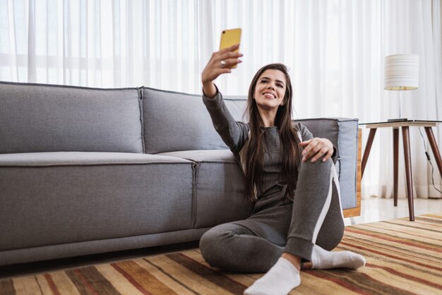 幸せなラテン女性は一人で家でリラックスする部屋のポーズに座るソーシャルメディアで良いニュースを共有する