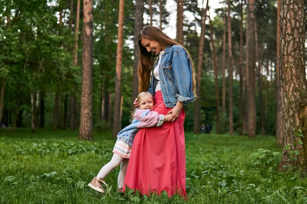 Happy laughing baby girl hugs her mom standing on the grass in the park