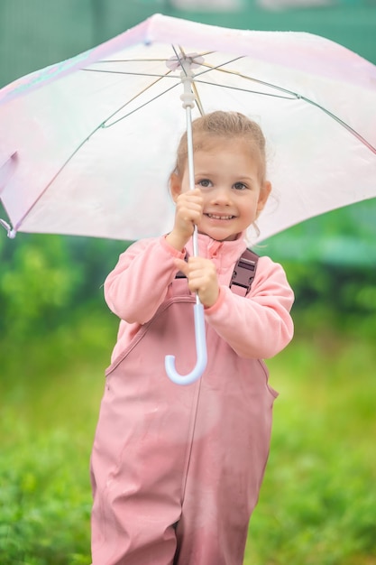 Happy laughing child girl year old wearing waterproof clothes and holding pink umbrella have a fun o