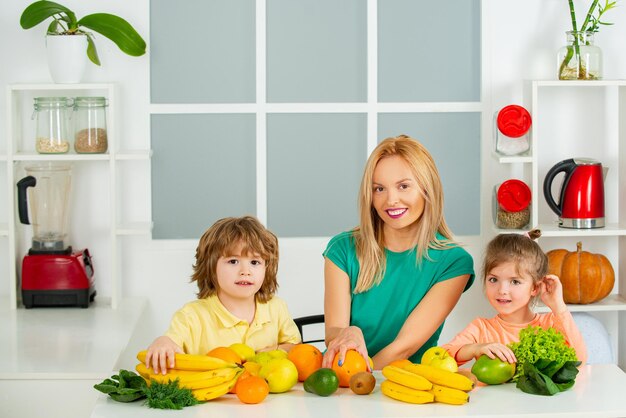 Happy laughing children and her beautiful young mother making fresh strawberry and other fruit juice...