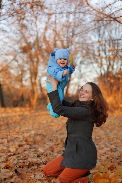 写真 笑う家族 母と子 娘が遊んで笑っている 秋の散歩 色とりどりの秋の公園で 葉の間で 幸せを表現している