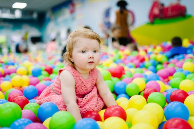 Счастливый смех девушка играет с игрушками, красочные шары на детской площадке, яма для мячей, сухой бассейн. Маленький милый ребенок, весело проводящий время в яме для мячей на вечеринке по случаю дня рождения в детском парке развлечений и игровом центре в помещении.
