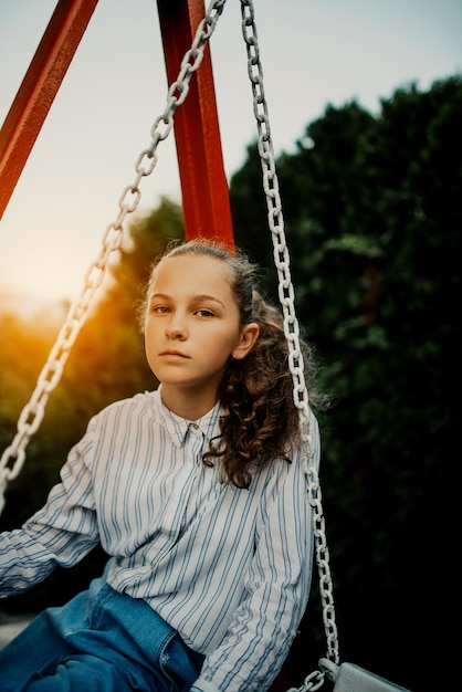 Happy laughing girl posing on swing in sunset summer