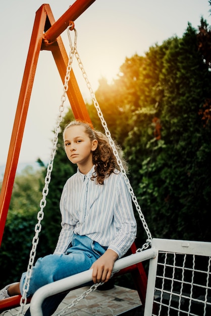 Happy laughing girl posing on swing in sunset summer