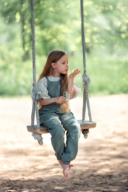 晴れた夏の日にブランコに乗って楽しんでいる長い髪の幸せな笑いの子供の女の子