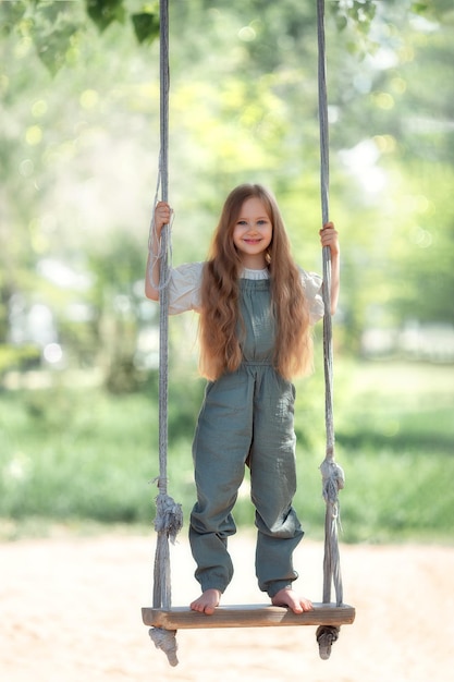 Счастливая смеющаяся девочка с длинными волосами, наслаждающаяся катанием на качелях в солнечный летний день