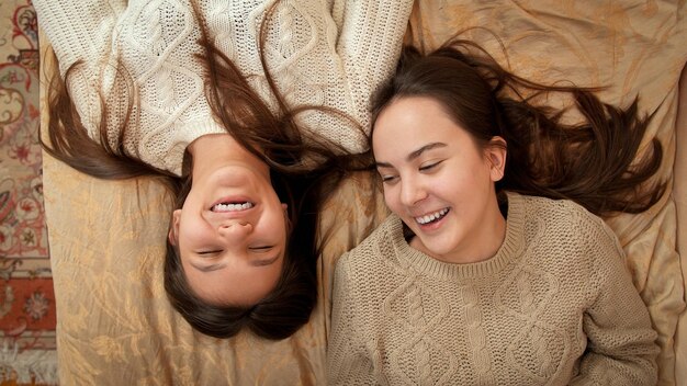 Happy laughing teenage girls lying together on bed and talking Teenager friendship and relationship