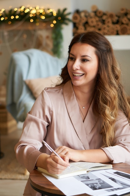 Happy laughing young woman at home making note in notebook