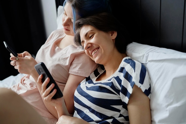 携帯電話でベッドに横たわっている幸せなレズビアンカップル
