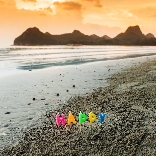 Happy letter candles in the sand with the mountains and the sea.