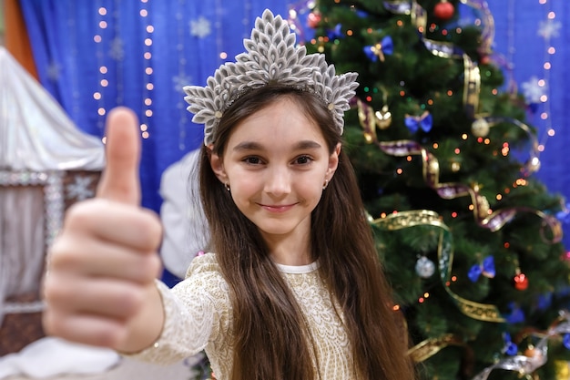 Happy little 10 years girl show thumb up sign ok looking at camera in christmas decorated home