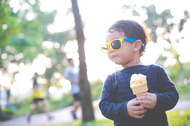 Happy little Asian boy eating ice cream cone with sun glasses in the garden, soft focus