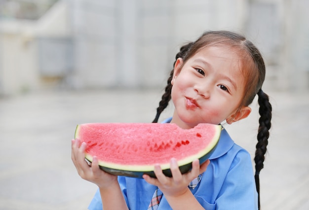 幸せなアジアの子供の女の子、学校の制服では、スイカの野外を楽しんでください。