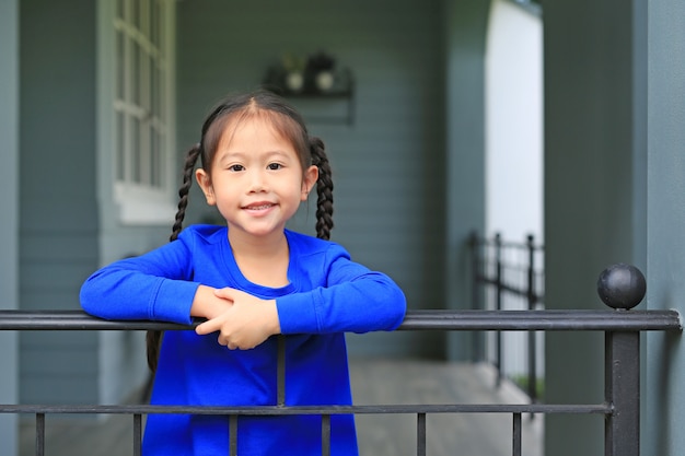 幸せの小さなアジア子供女の子家のバルコニーのバーに立っていると朝のカメラ目線します。