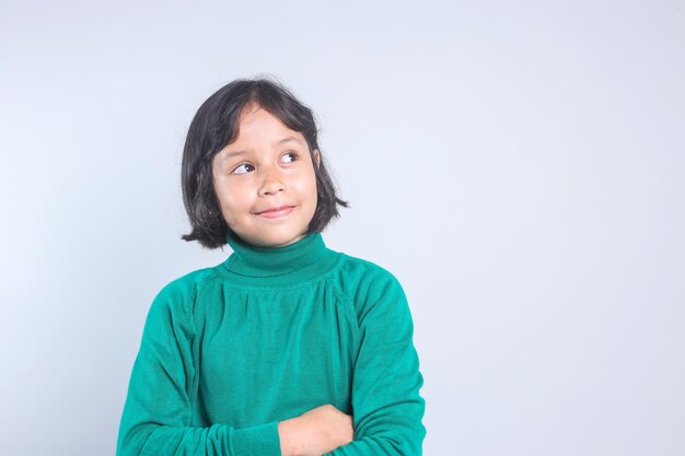 Happy little Asian girl looking up to the empty space over grey background