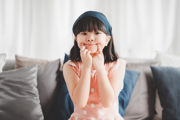 Happy little asian girl making funny face using fingers  touch her mouth