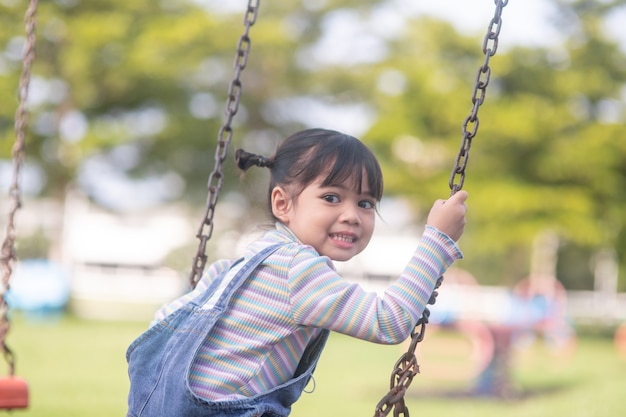 Happy little Asian girl playing swing outdoor in the park