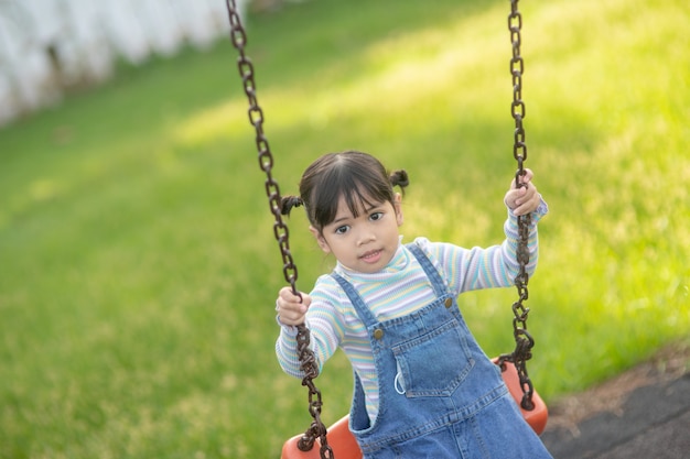 公園で屋外のブランコを遊んで幸せな小さなアジアの女の子