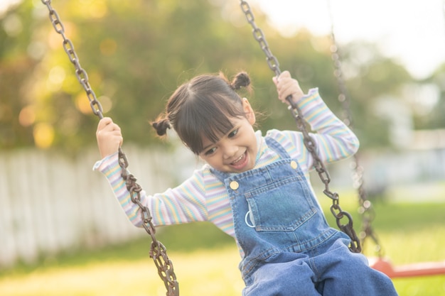 Foto felice piccola ragazza asiatica che gioca a swing all'aperto nel parco