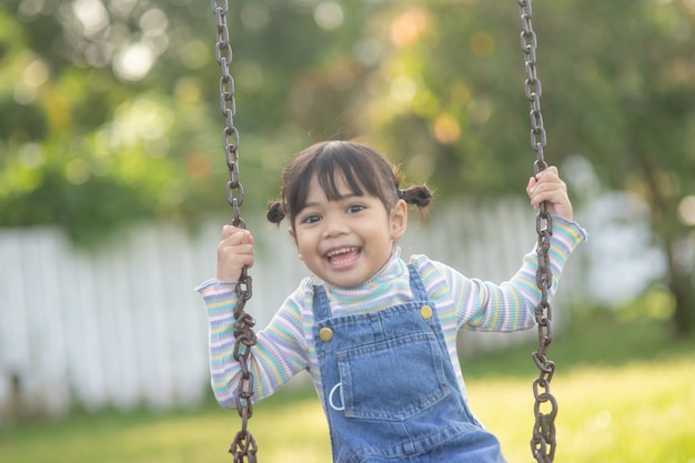 Happy little Asian girl playing swing outdoor in the park