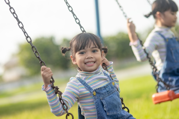 Счастливая маленькая азиатская девушка играет на качелях на открытом воздухе в парке