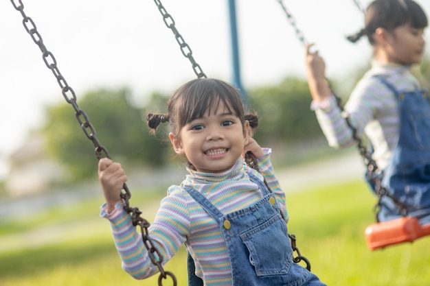 Happy little Asian girl playing swing outdoor in the park