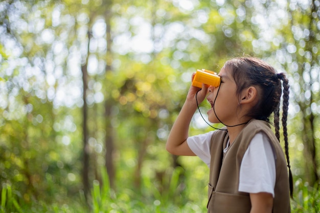 Happy Little Asian girls looking ahead and smiling child with the binoculars in the park Travel and adventure concept Freedom vacation