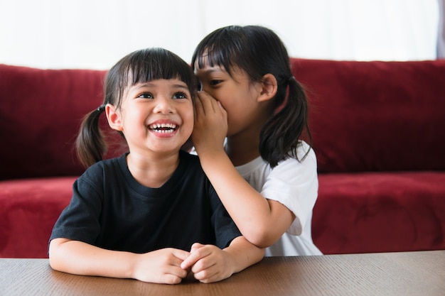 Happy little Asian siblings sharing secrets