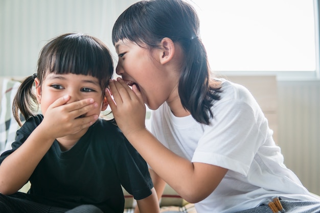 Happy little Asian siblings sharing secrets