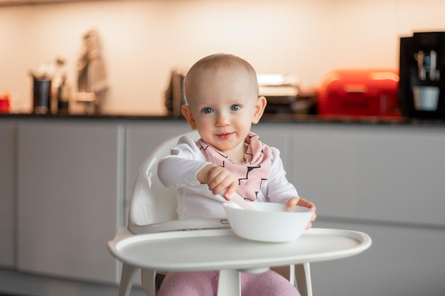 Happy little baby eats on his own with a spoon while sitting in a high chair